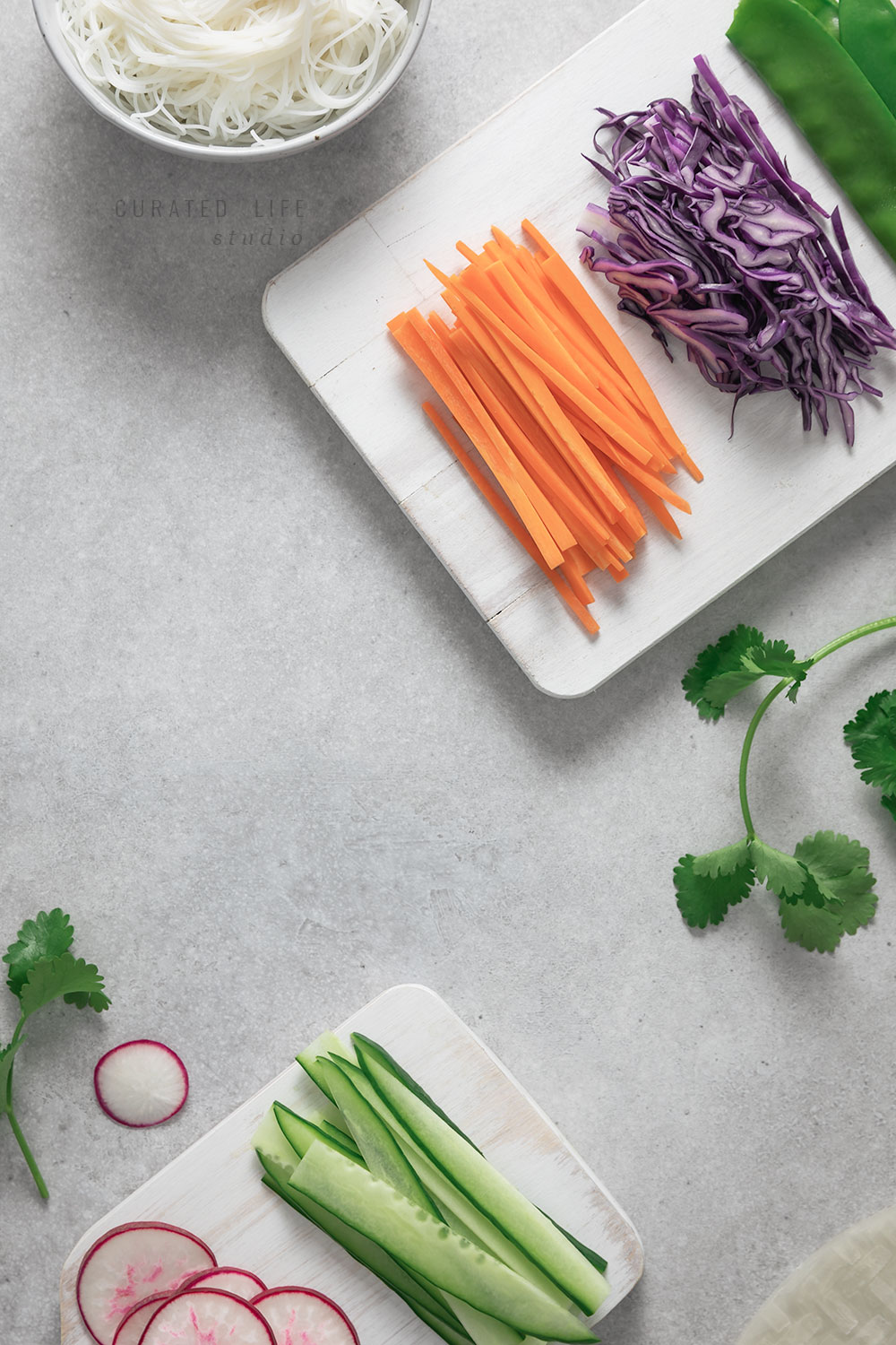 Birds eye view of two white chopping boards filled with recently chopped carrot sticks, cabbage, cucumber slices and radishes. 

#Vietnamese #Healthy #Peanut #Dipping #Sauce #Vegetarian #Vegan #Gluten-free #Tofu #Recipe #Rice #Paper #Spring #Rolls #Fresh